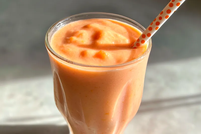 A vibrant Tropical Sunrise Sunset Smoothie being poured into a glass, showcasing its creamy texture and bright colors.