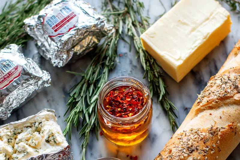 Close up of hot honey being drizzled over white whipped cheese dip with rosemary garnish